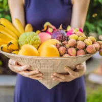 Woman holds a variety of tropical fruits and vegetables in 2025